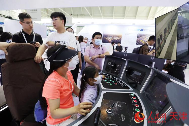 一位參觀者和孩子在天津軌道交通集團(tuán)展臺體驗(yàn)智能駕駛帶來的樂趣。人民網(wǎng)記者 孫翼飛攝